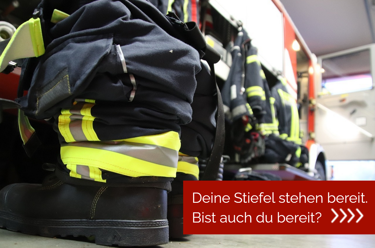 Ein paar schwarze Stiefel stecken in einer schwarzen Hose, im Hintergrund sieht man ein rotes Feuerwehrauto.