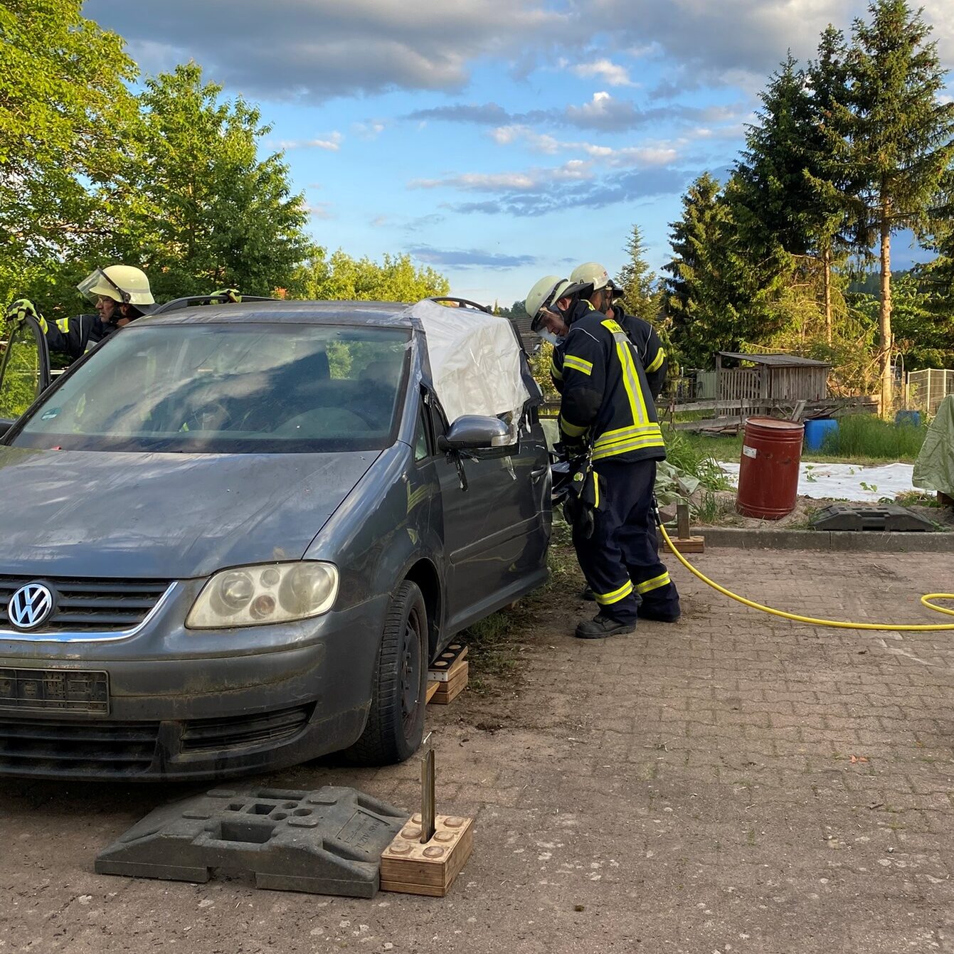Zwei Feuerwehrmänner stehen an einem Auto und beginnen mit einem hydraulischen Spreizer die Fahrertür zu öffnen.