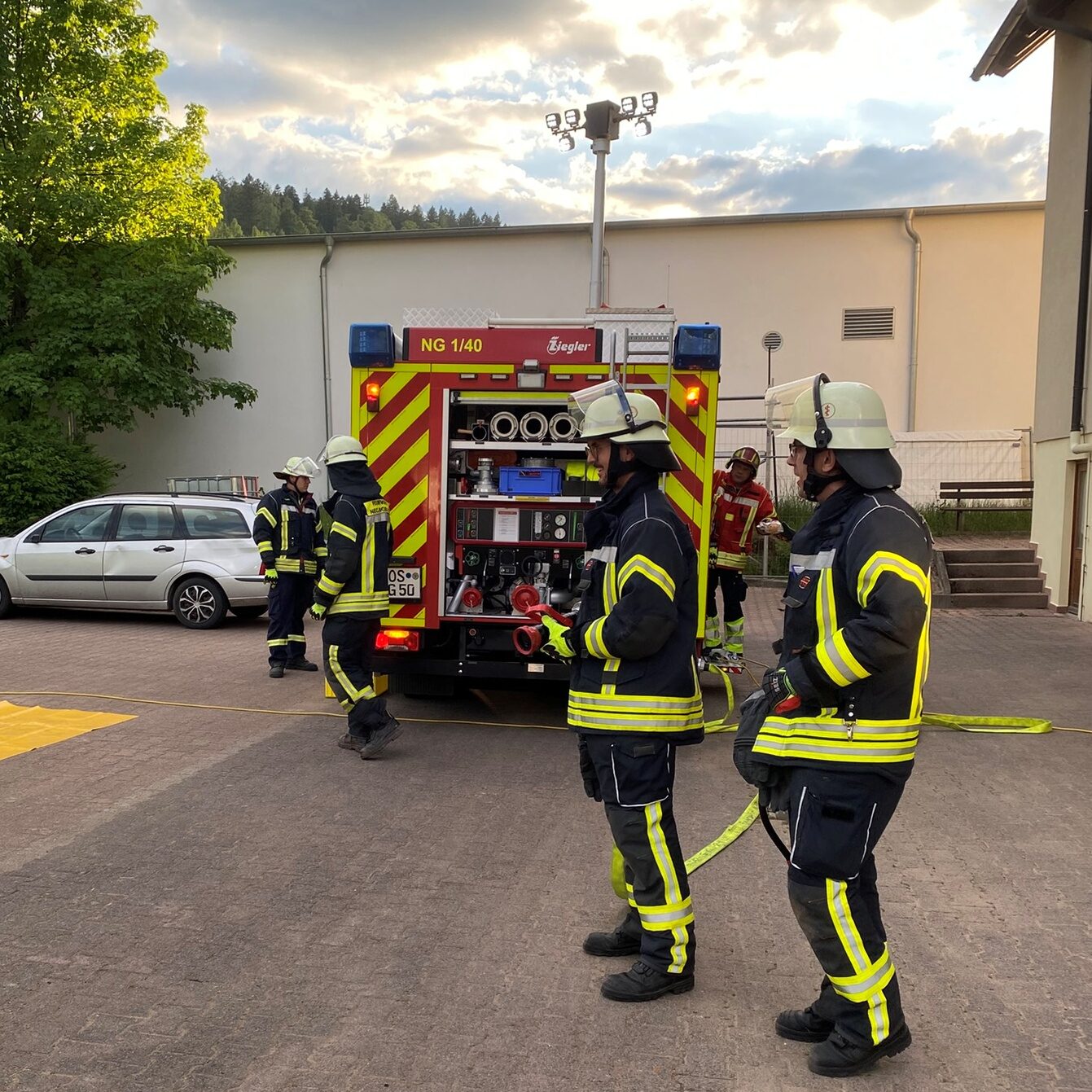 Mehrere Feuerwehrmänner stehen um das Feuerwehrauto herum. Einer hält ein Strahlrohr in der Hand.