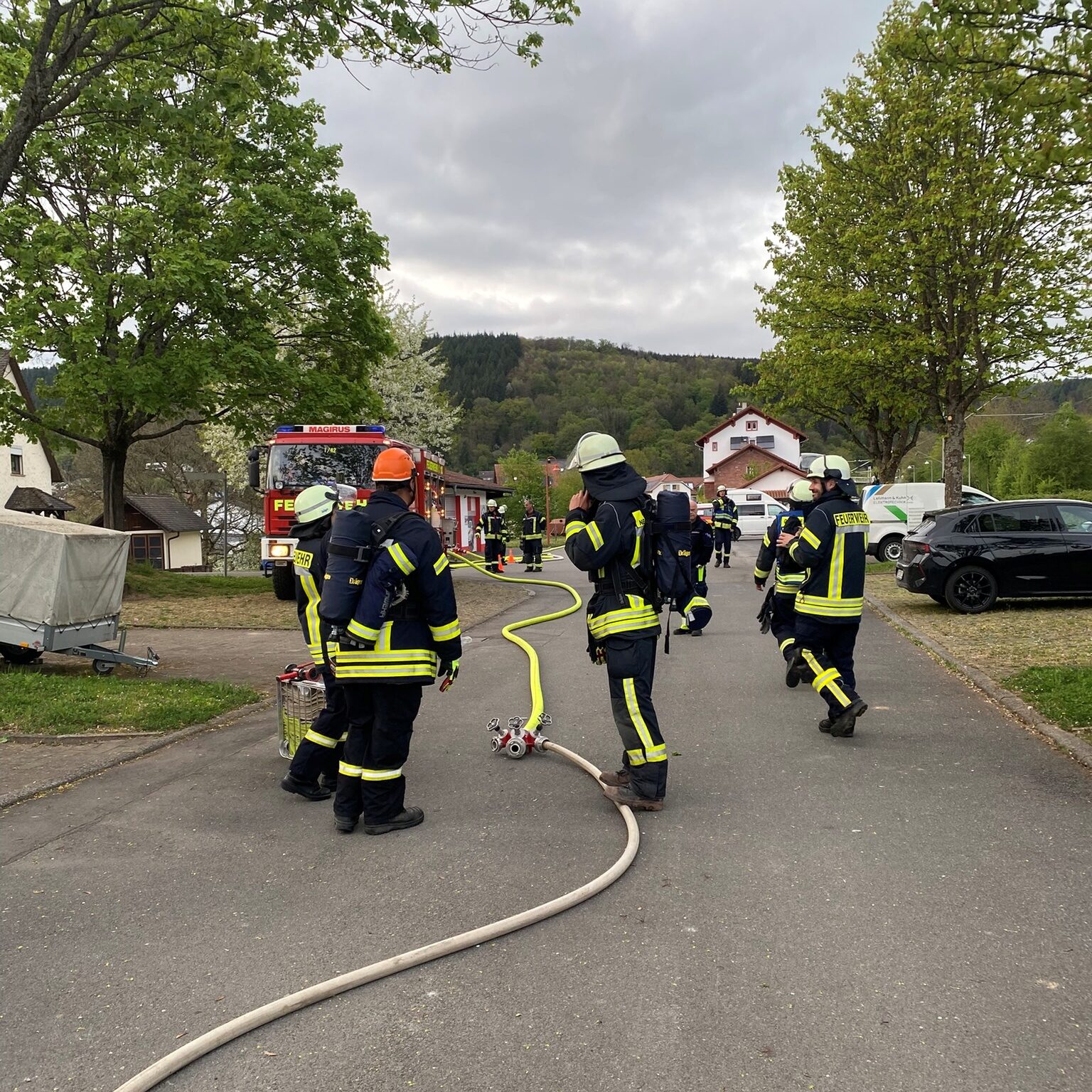 Mehrere Feuerwehrleute stehen auf der Straße, im Hintergrund ein rotes Feuerwehrauto.
