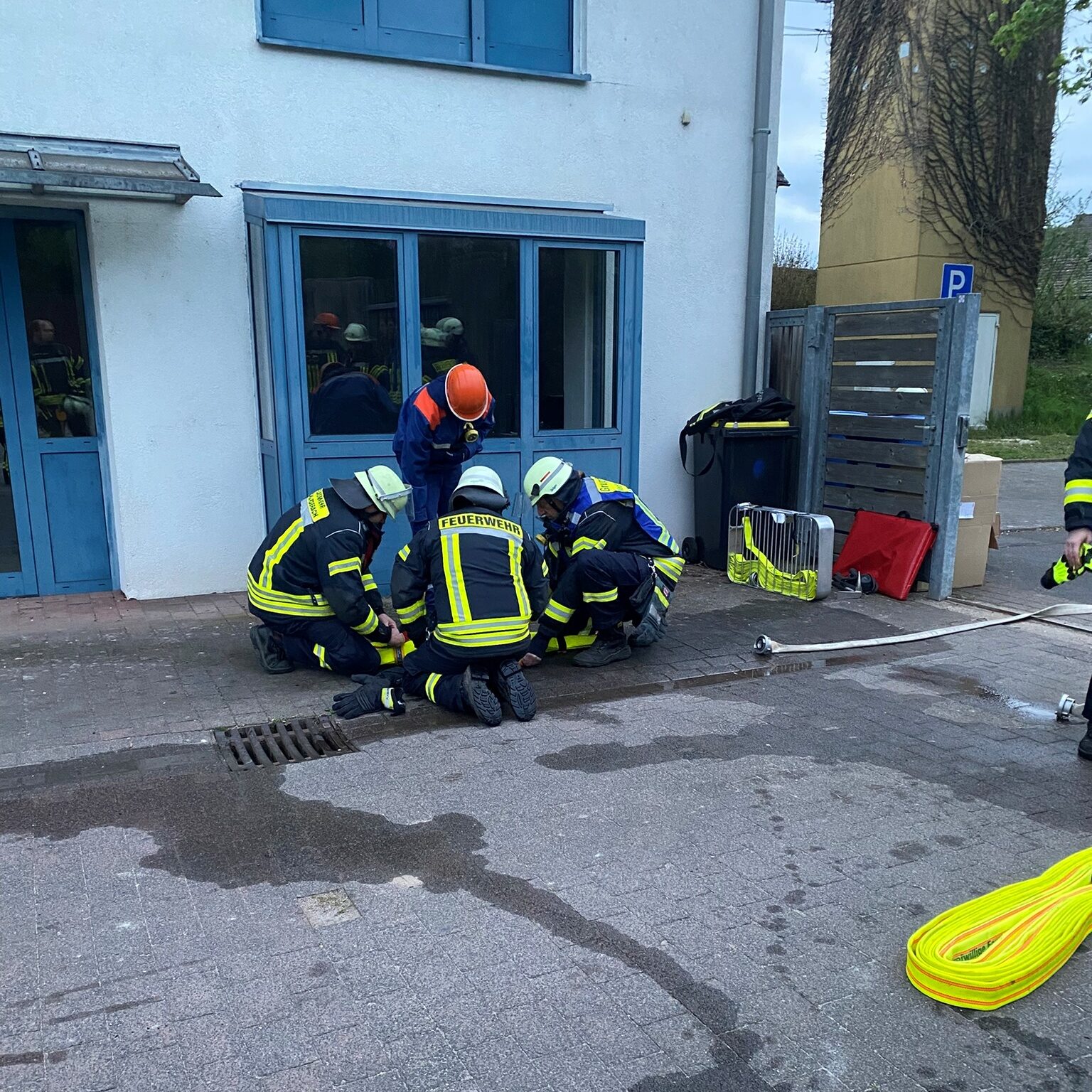 Drei Feuerwehrleute und ein Mitglied der Jugendfeuerwehr mit orangenem Helm knien auf dem Boden.