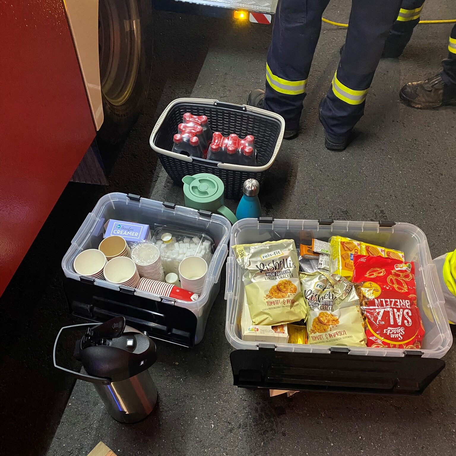 Auf dem Boden stehen Körbe und Kisten mit Getränken, Verpackungen von Snacks und Becher zum Trinken.