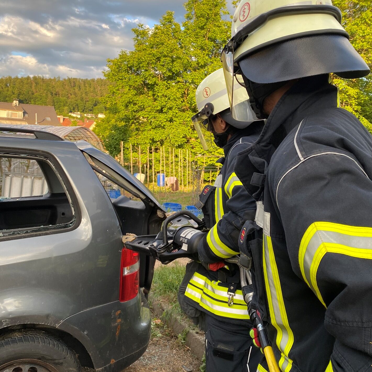 Ein Feuerwehrmann öffnet mit einem hydraulischen Spreizer den Kofferraum eines grauen Autos.