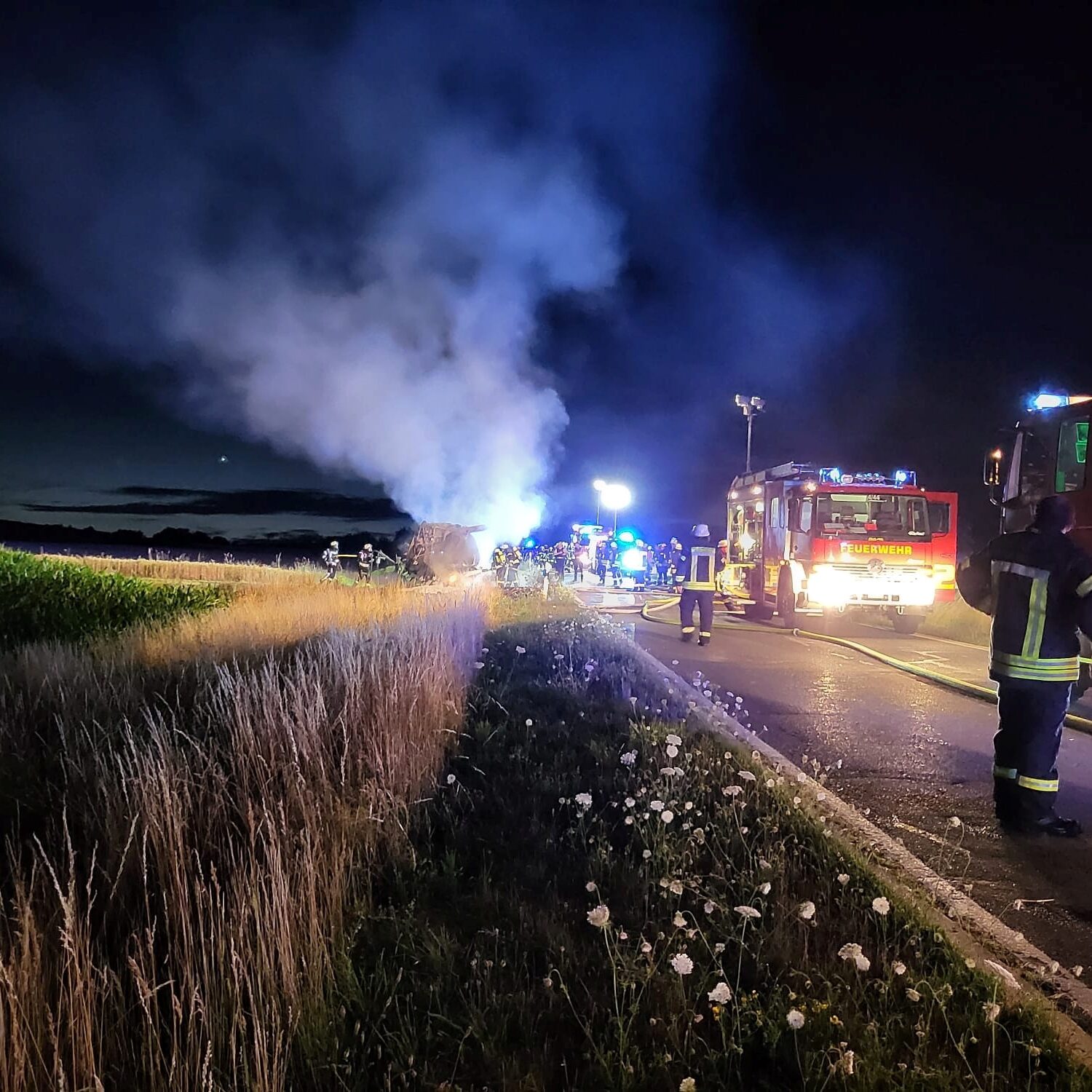 Nachts steigt Rauch von einem Brand auf. Auf der Straße daneben stehen mehrere Feuerwehrautos.