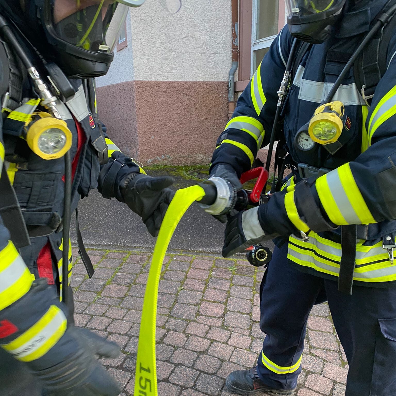 Ein Feuerwehrmann hält ein Strahlrohr, während ein anderer Feuerwehrmann den Schlauch daran befestigt.
