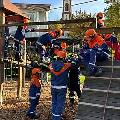 Kinder in blauen und orangenen Uniformen stehen und sitzen auf einem Klettergerüst auf einem Spielplatz.