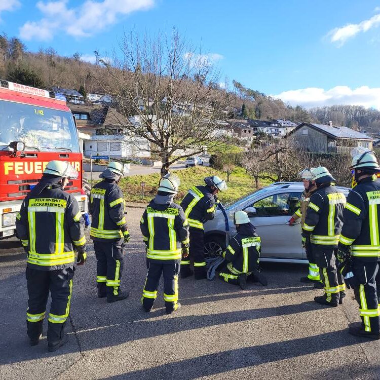 Eine Gruppe Feuerwehrleute mit Schwarz-Gelben Jacken stehen um ein silbernes Auto herum.