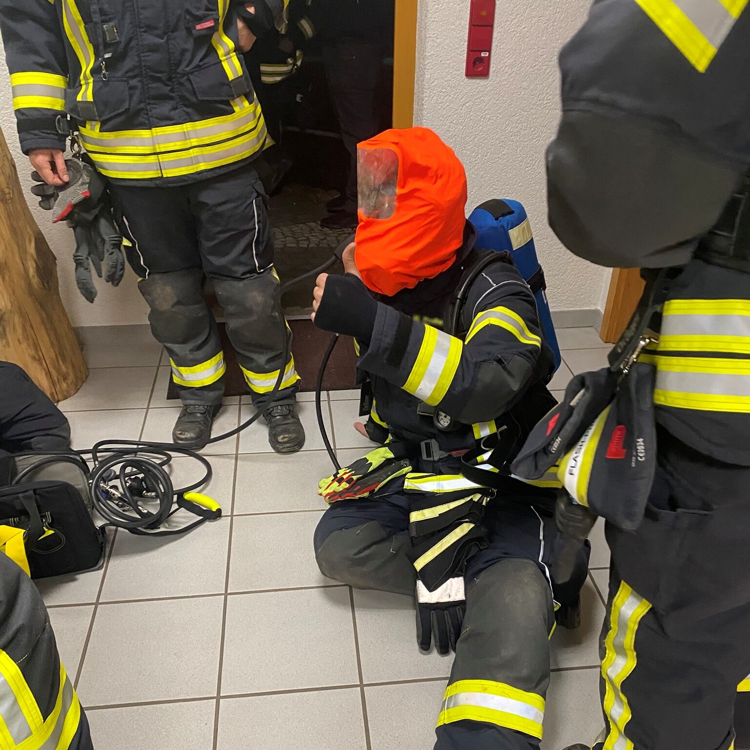 Ein Feuerwehrmann sitzt auf dem Boden und hat eine rote Maske übergezogen.