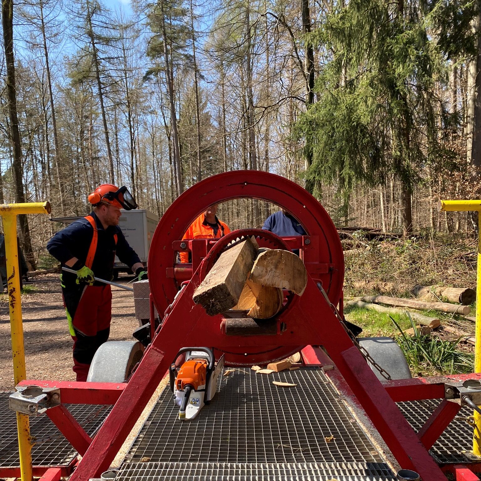 Blick in ein rundes Gerät, in dem mehrere Stücke Holz eingespannt sind, daneben steht eine Person.