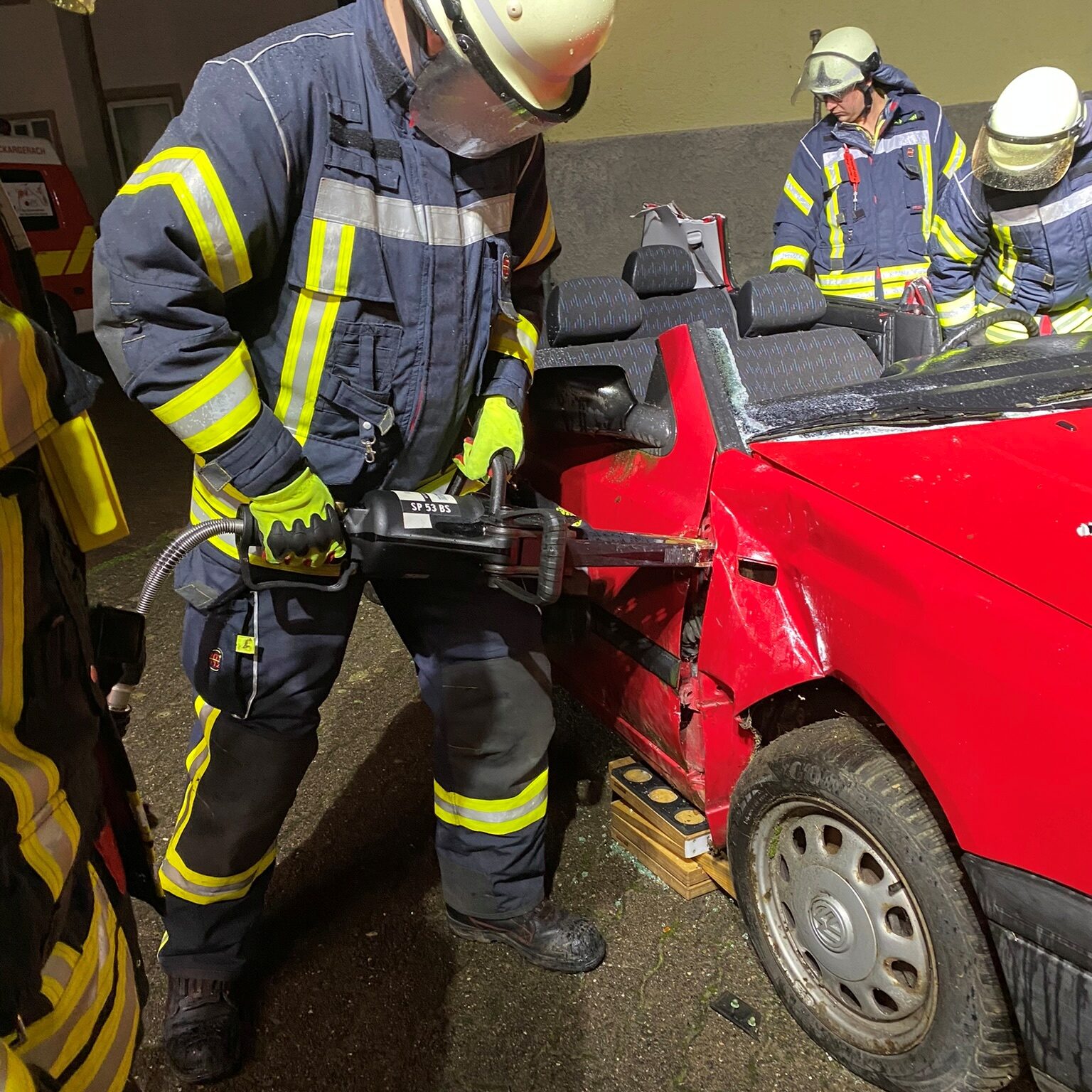 Ein Feuerwehrmann drückt mit einem Rettungsgerät in einen Spalt an einem roten Auto.